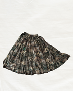 A pleated A-line skirt with a dark camouflage pattern featuring shades of brown, green, and black, laid flat on a white background.