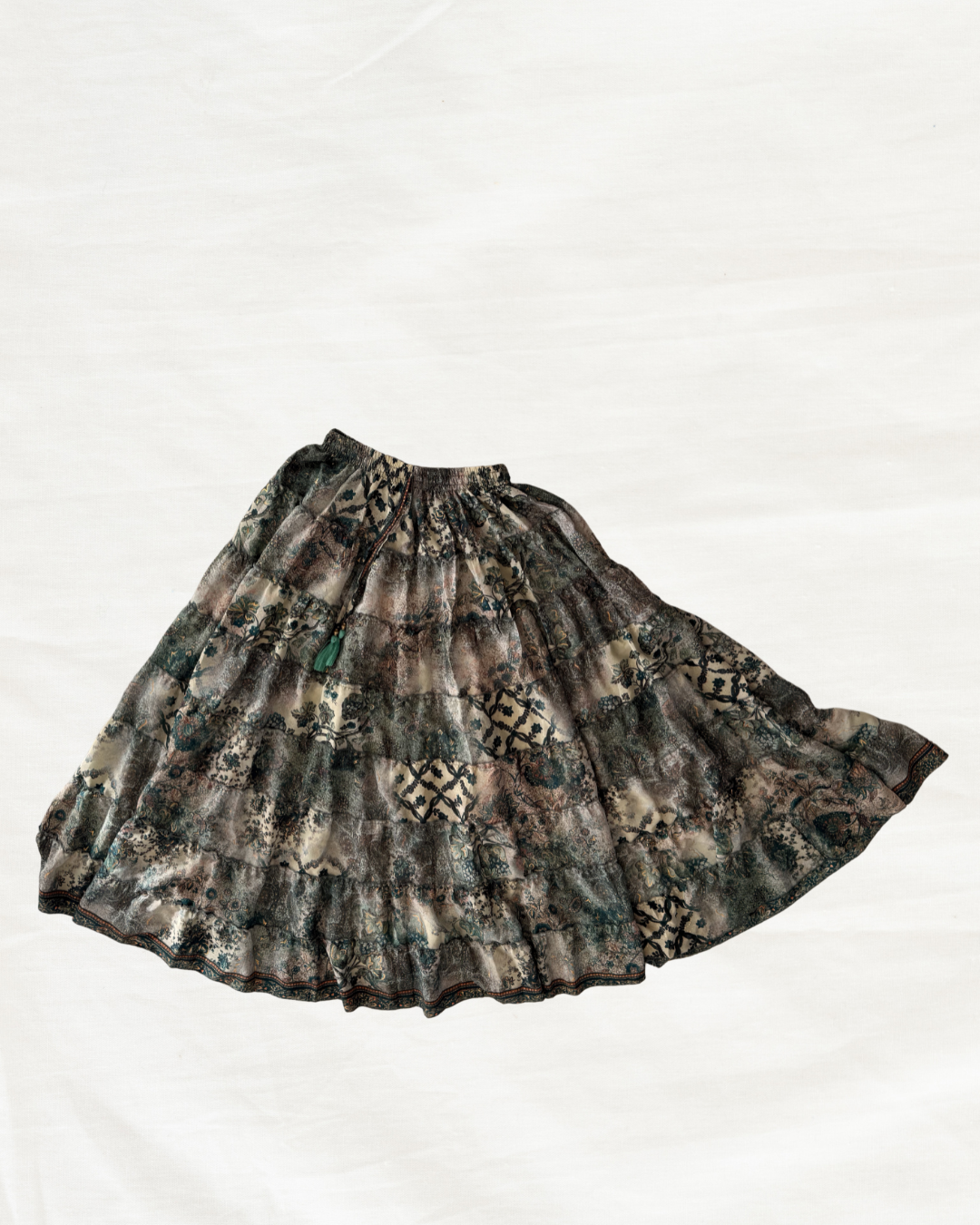 A pleated A-line skirt with a dark camouflage pattern featuring shades of brown, green, and black, laid flat on a white background.