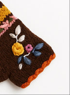 A pair of brown knit fingerless gloves with colorful striped bands and floral embroidery, displayed on a clean white background.