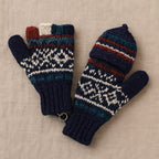 A pair of hand-knit winter mittens with a Fair Isle pattern in navy blue, teal, white, and rust red, displayed on a neutral beige fabric background.