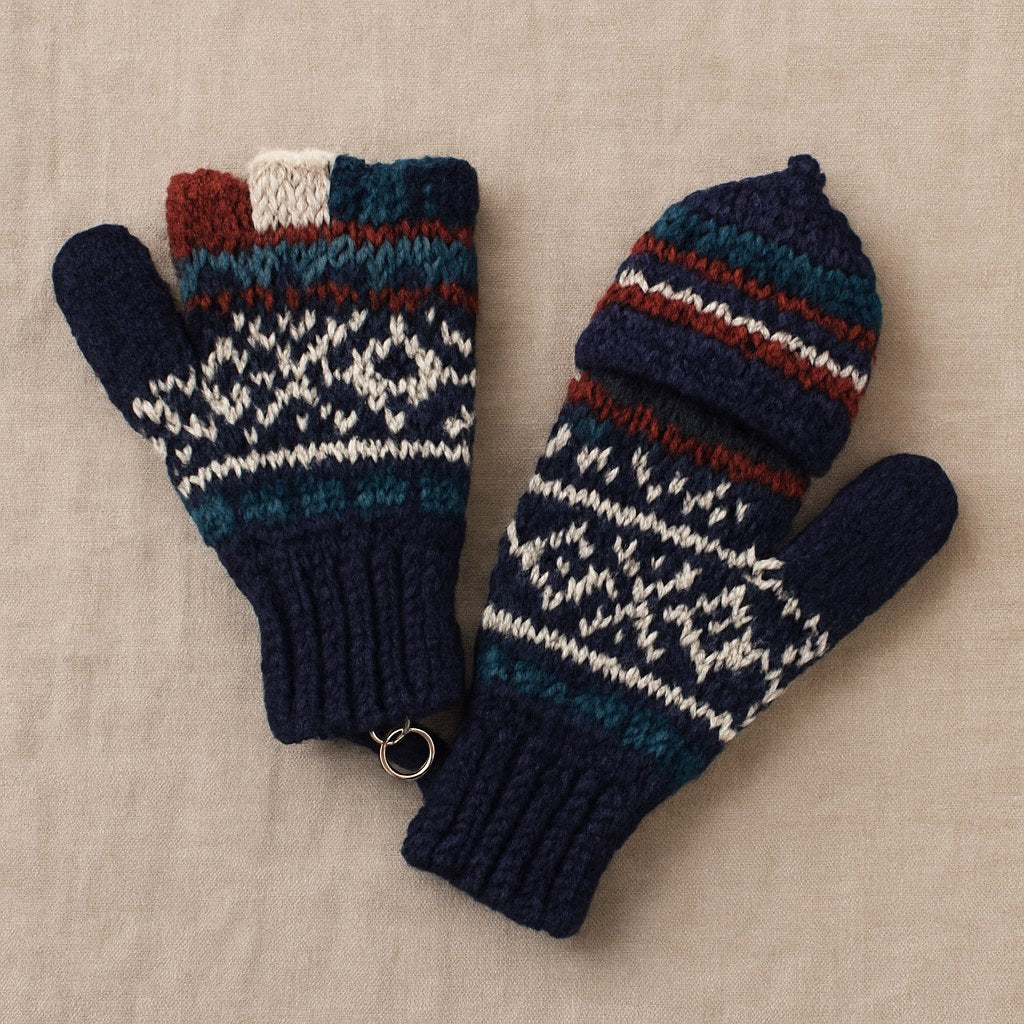 A pair of hand-knit winter mittens with a Fair Isle pattern in navy blue, teal, white, and rust red, displayed on a neutral beige fabric background.