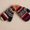 A pair of hand-knit winter mittens with a multicolor Fair Isle pattern of navy blue, red, beige, and white, displayed on a neutral beige fabric background.